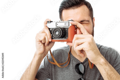 Portrait of a handsome photographer guy with a beard, taking pictures with a camera standing on a white background
