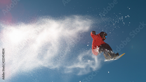 SLOW MOTION: Snowboarder jumping big air, snowflakes flying behind him in winter