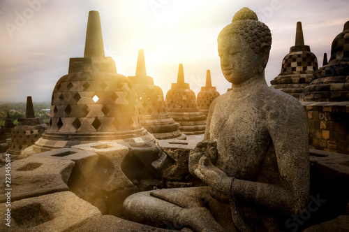 View of meditating Buddha statue and stone stupas against sunrise. Great religious architecture. Magelang, Central Java, Indonesia photo