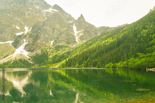 A beautiful view of the 'Morskie Oko' lake in the Polish Mountains in the Tatras. Green trees are reflected from the water's surface. A beautiful landscape from the perspective of a tourist.
