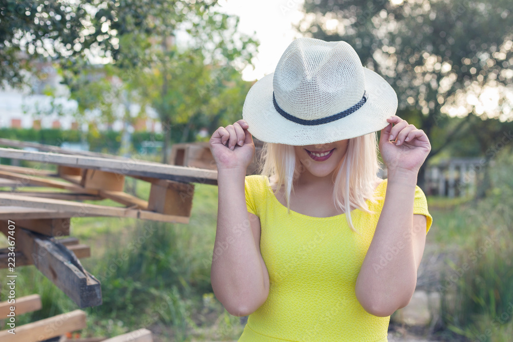 Blonde woman mocking up with a white hat. Smiling, outdoors, on a sunny day.