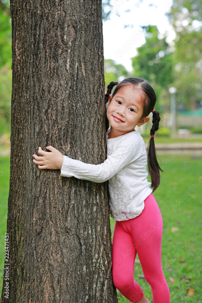 Child girl hugging a tree with looking at camera in park. Child girl hugging a tree with looking at camera in park.