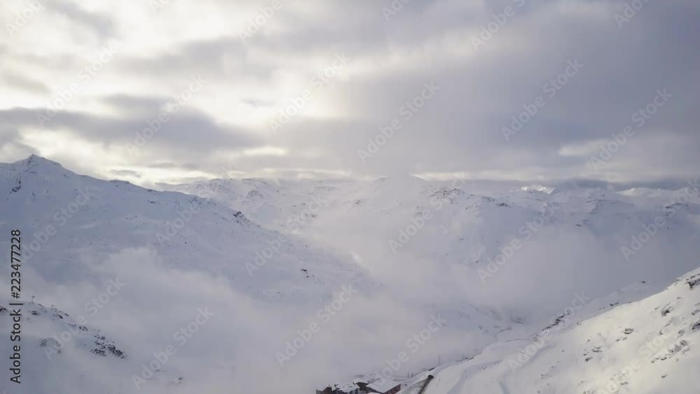 Spectacular winter landscape of snow covered mountains beautifully surrounding small modern ski resort containing lots of colorful houses, long tracks, ski parks, moving skiers and snowboarders