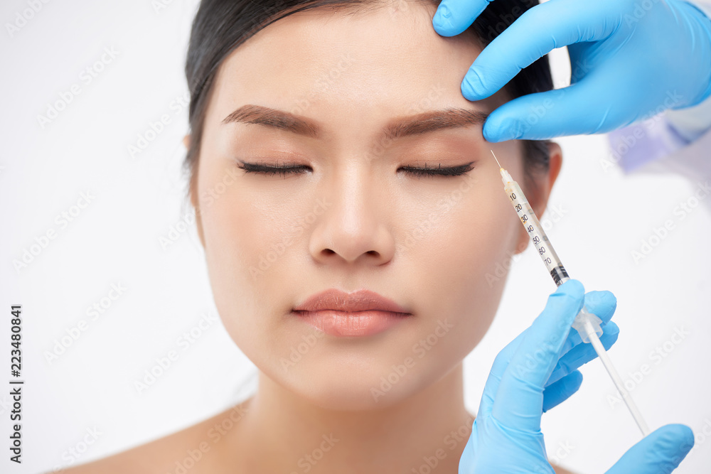 Young Asian woman getting rejuvenating botox injection under brow