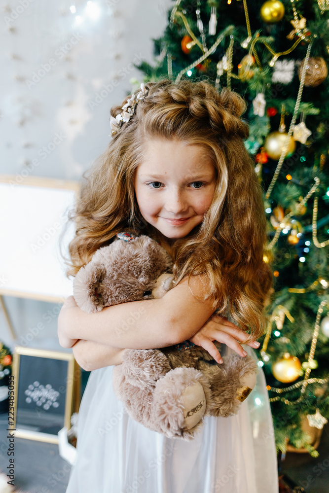 little sweet girl sits under a Christmas tree with a soft toy teddy bear little sweet girl sits under a Christmas tree with a soft toy teddy bear