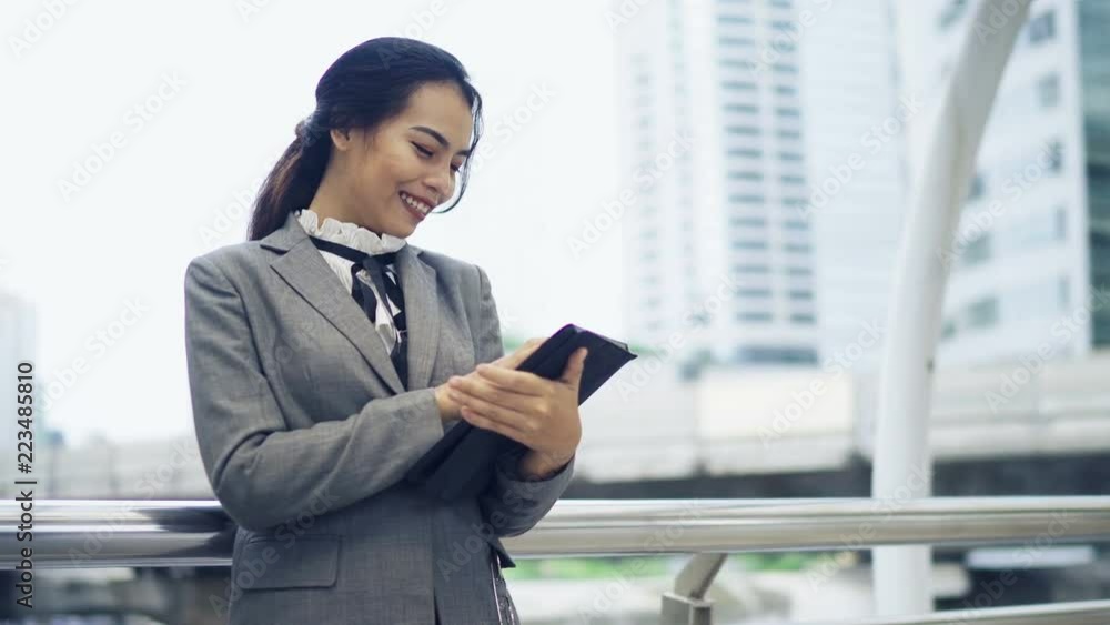 Asian businesswoman standing outside the office and using her tablet for working. Asian businesswoman standing outside the office and using her tablet for working.