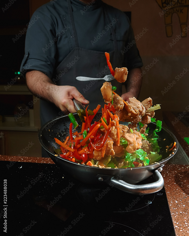 Caucasian chief cook cooking on the wok pan.Vegetables are flying Photos |  Adobe Stock