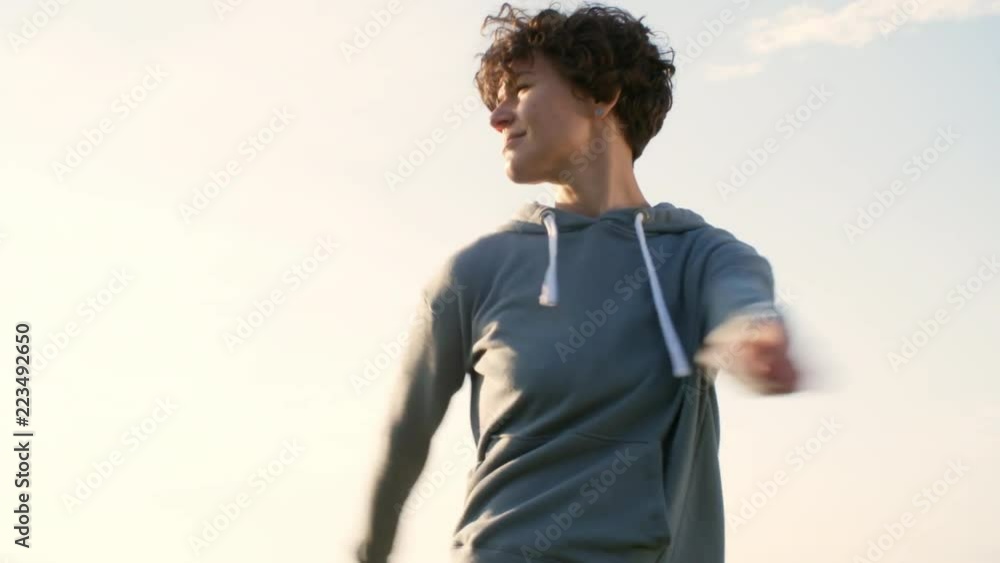 Young woman in sports hoodie doing neck and torso rotation exercises in the park at sunny summer day Young woman in sports hoodie doing neck and torso rotation exercises in the park at sunny summer day