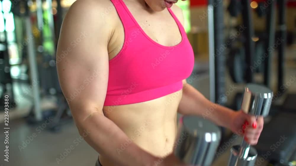 Muscular athlete woman in a pink top working out in the gym lifting weights. Fitness girl exercising in the gym with dumbbells. The concept of sport, beauty, fitness, healthy lifestyle, beautiful body Muscular athlete woman in a pink top working out in the gym lifting weights. Fitness girl exercising in the gym with dumbbells. The concept of sport, beauty, fitness, healthy lifestyle, beautiful body