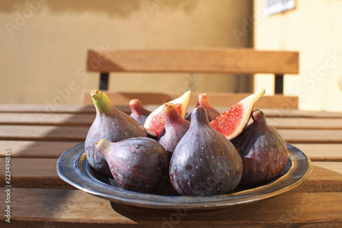 Fresh figs on ceramic black plate Wooden table Sunligh Copy space Autumn harvesting Fall