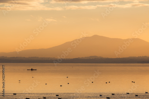 Beautiful view of a lake at sunset  with orange tones  birds on water and a man on a canoe