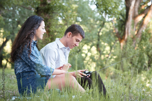 young couple sitting on the grass in the forest and looking on sunset, listen to radio, summer nature, bright sunlight, shadows and green leaves, romantic feelings