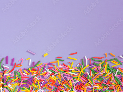 Border frame of colorful sprinkles on lilac purple background with copyspace. Top view or flat lay