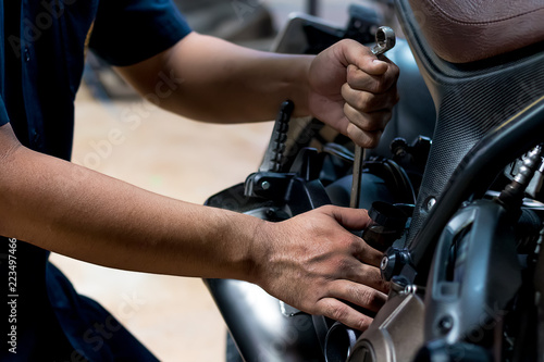 People are repairing a motorcycle Use a wrench and a screwdriver to work. Use the wrench to tighten the cylinder. © Suppasit