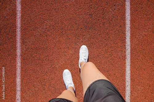 Tableau sur toile Young woman's legs in white shoes standing on stadium track in summer day
