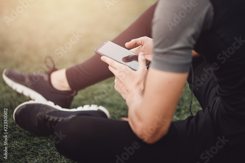 Young handsome man using phone while having exercise break in on football field with green lawn.
