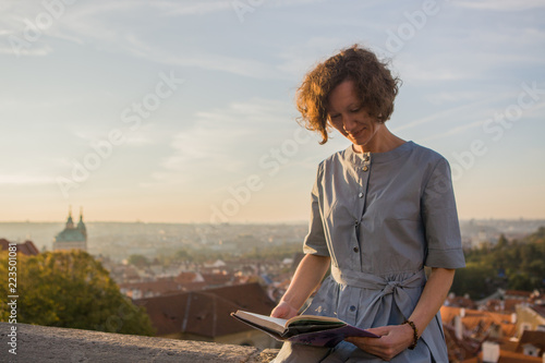 Photography Woman on a sunny day sitting and reading a book on a panorama background Prague,