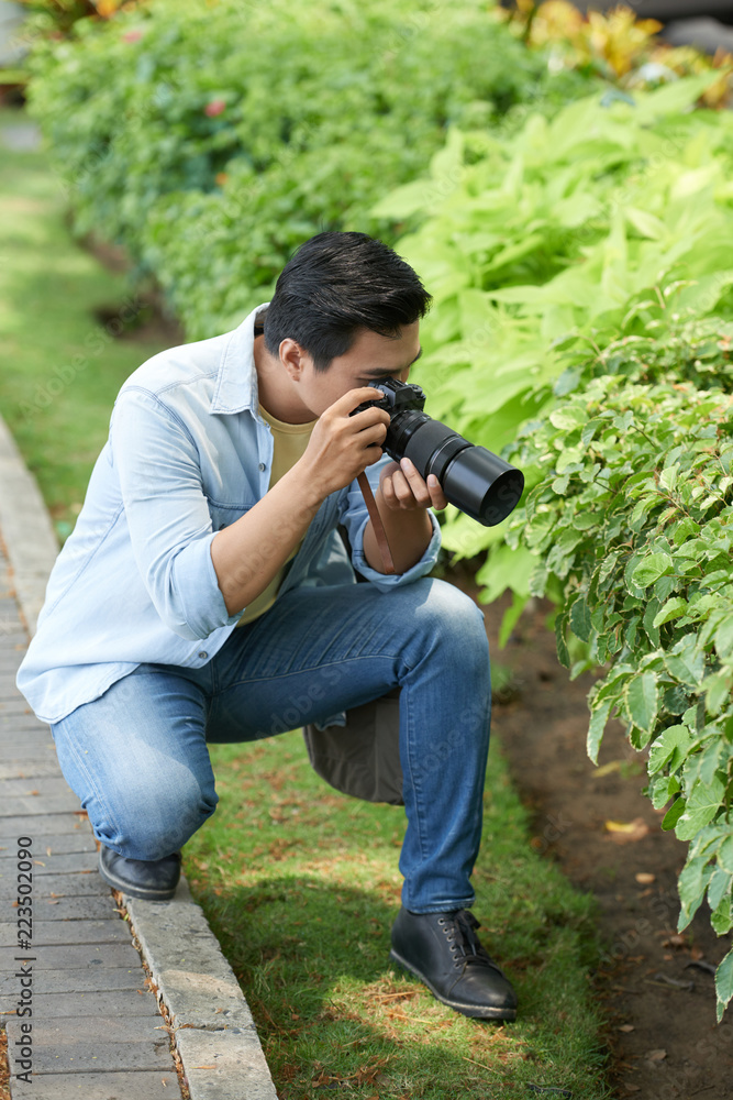 Young man photographing leaves and bushes in park