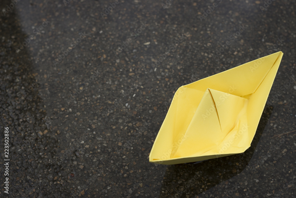 Yellow paper boat on wet asphalt, mood concept, copy space