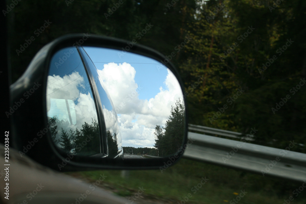 the road, sunny summer sky with clouds and trees reflection in car side mirror as travel background