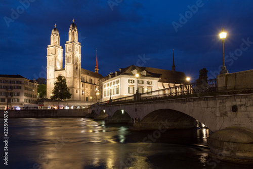 Beautiful cityscape of Zurich, Switzerland, with the Grossmünster Protestant church and the Helmhaus museum, seen from the shore of the river Limmat in the blue hour in summer 