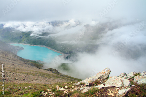 Beautiful view from above of the vibrant turquoise reservoir lake Lac de Moiry in the alps near Grimentz, Switzerland, on a cloudy summer day in the mountains