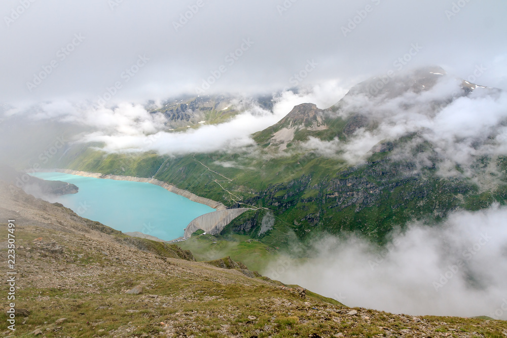 Beautiful view from above of the vibrant turquoise reservoir lake Lac de Moiry in the alps near Grimentz, Switzerland, on a cloudy summer day in the mountains