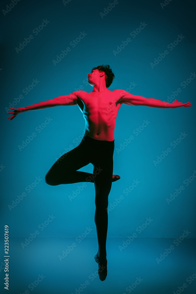 The male athletic ballet dancer performing dance on dark blue background. Studio shot. Ballet concept. Fit young man. Caucasian model