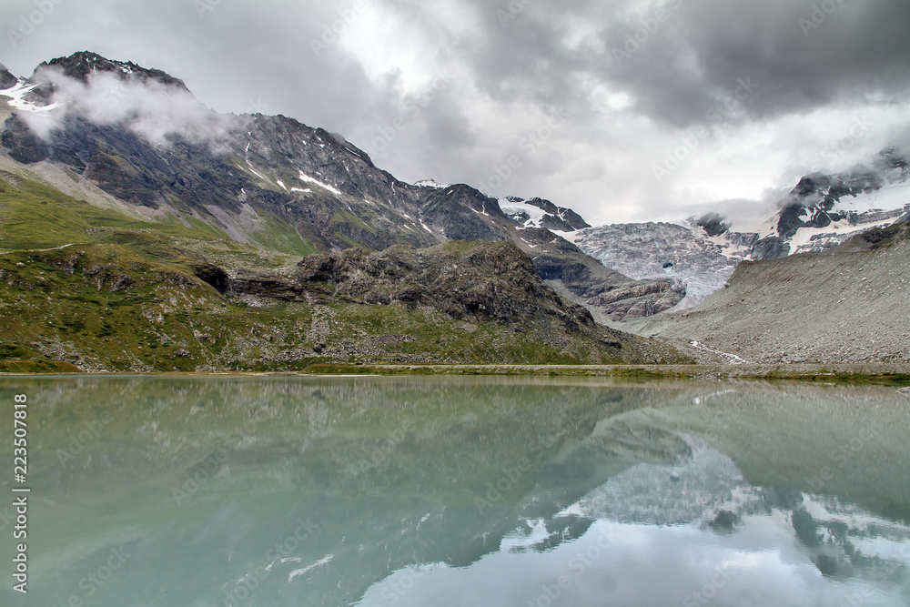 Beautiful landscape view of the Moiry glacier reflected in a milky blue lake of melted ice with a ominous sky with clouds in summer in the Swiss pennine alps near Grimentz, Valais, Switzerland