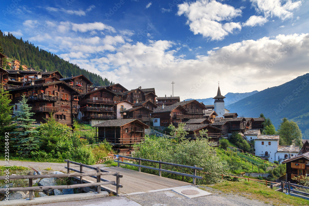 Beautiful cityscape of the alpine village Grimentz, Switzerland, with traditional wooden houses and church tower in summer
