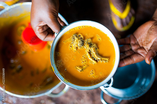 hands of cameroonian woman holding pot of traditional taro with sauce jaune dish in african kitchen photo