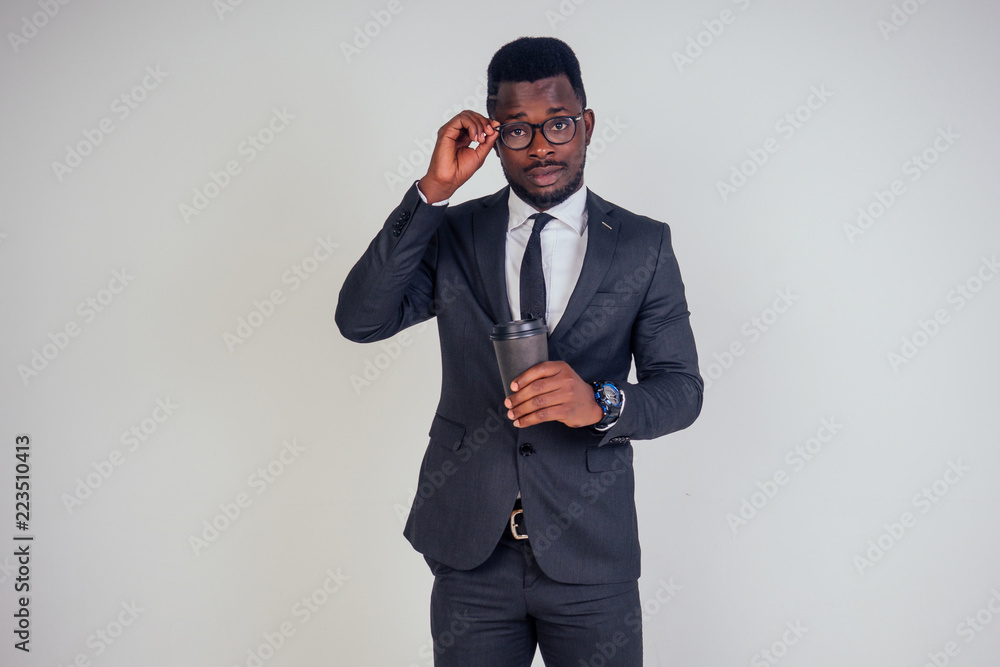 Handsome young African man in formal black suit holds a plastic paper cup with hot coffee cocoa (tea) to go . businessman on coffee break after meeting on white background in studio Handsome young African man in formal black suit holds a plastic paper cup with hot coffee cocoa (tea) to go . businessman on coffee break after meeting on white background in studio