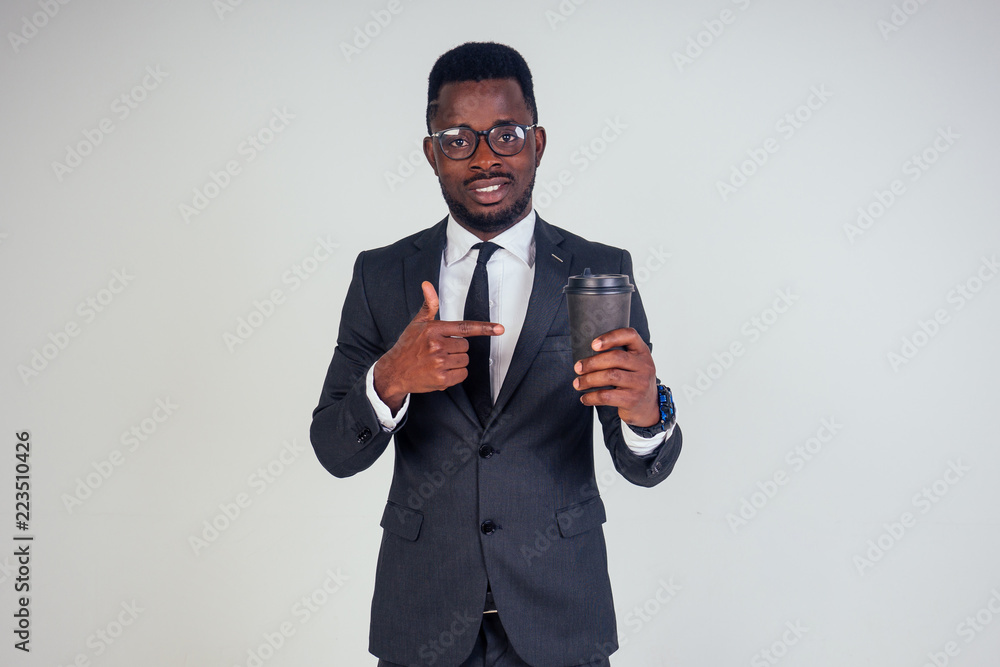 Handsome young African man in formal black suit holds a plastic paper cup with hot coffee cocoa (tea) to go . businessman on coffee break after meeting on white background in studio Handsome young African man in formal black suit holds a plastic paper cup with hot coffee cocoa (tea) to go . businessman on coffee break after meeting on white background in studio
