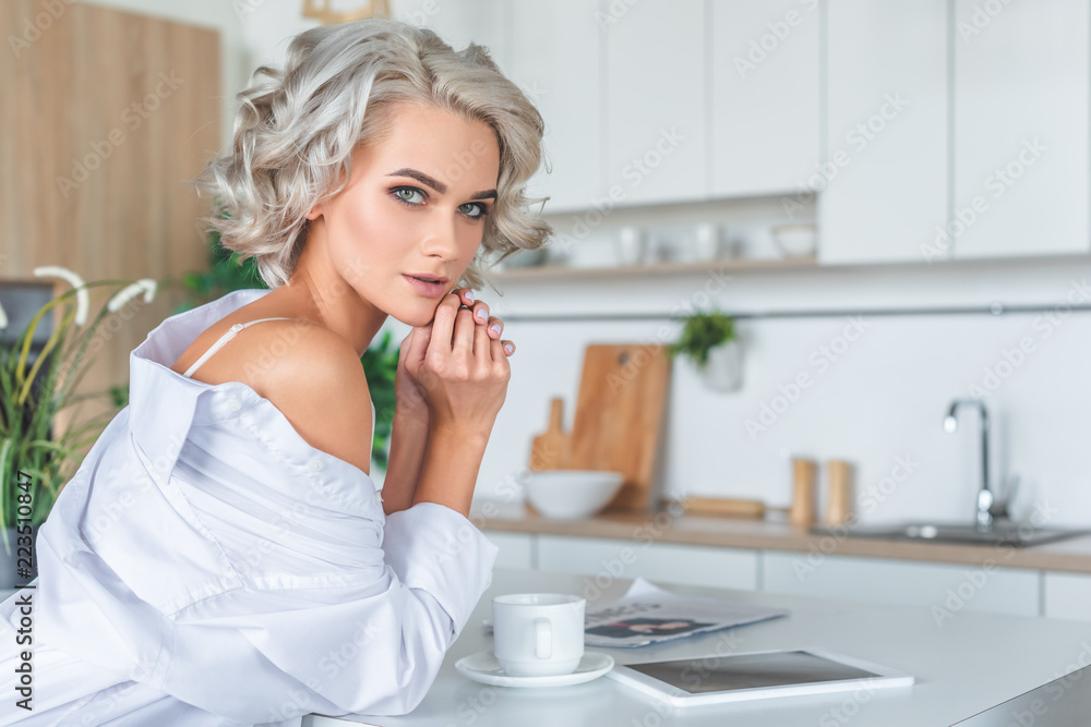 attractive young woman in white shirt with tablet and coffee cup at kitchen in morning attractive young woman in white shirt with tablet and coffee cup at kitchen in morning
