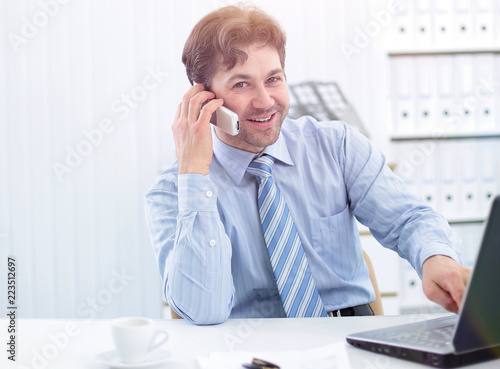 handsome businessman sitting at Desk and talking on a cell phone