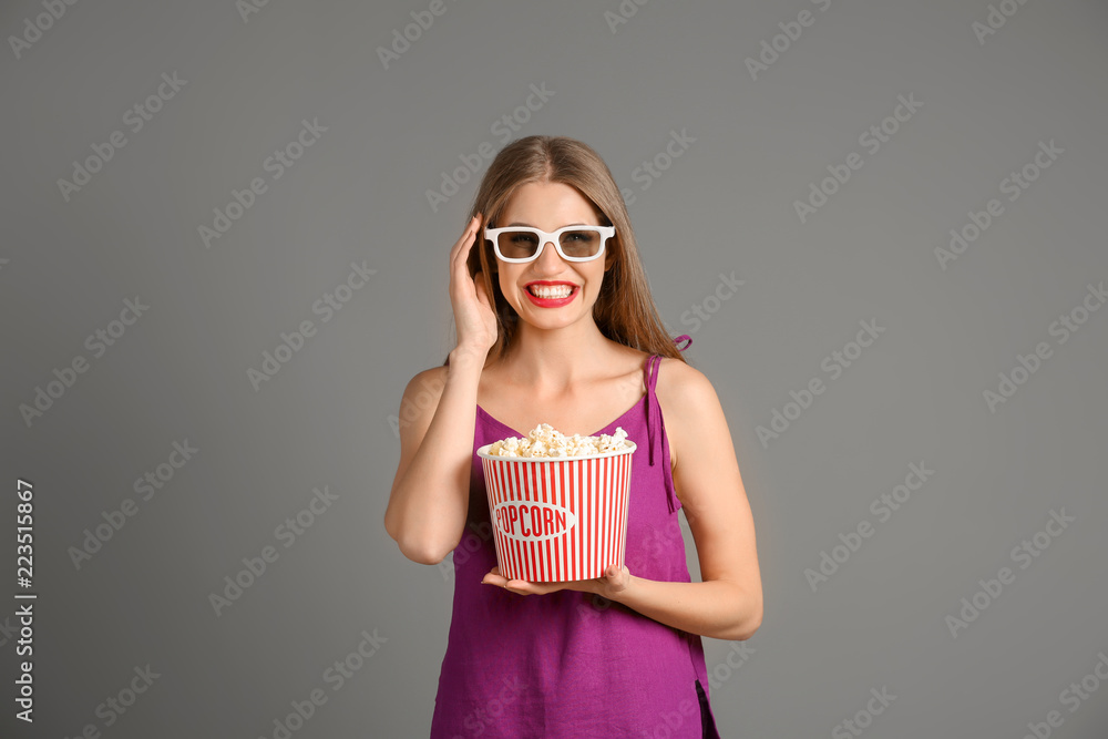 Beautiful young woman with cup of popcorn and 3D cinema glasses on grey background Beautiful young woman with cup of popcorn and 3D cinema glasses on grey background