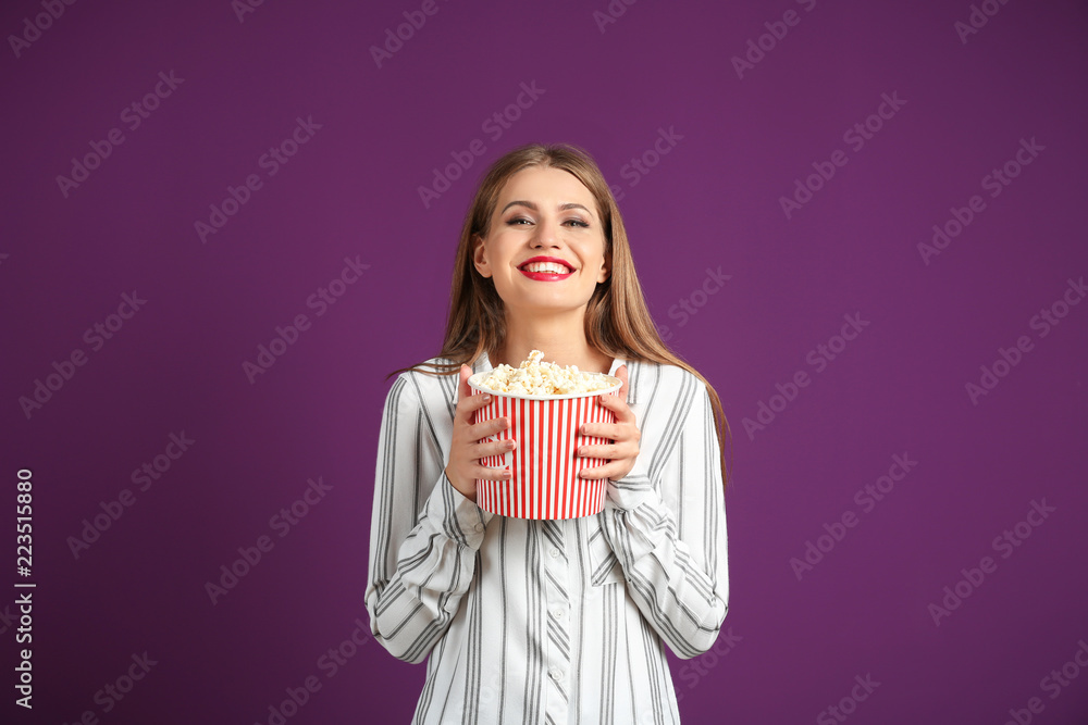 Beautiful young woman with cup of popcorn on color background Beautiful young woman with cup of popcorn on color background
