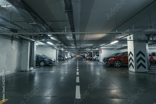 Large hall with columns of underground car parking garage with many automobiles in modern mall or shopping center inside