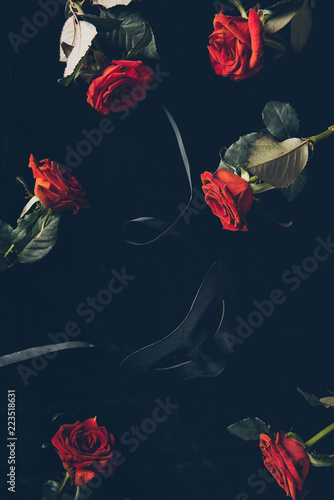 Fototapeta Naklejka Na Ścianę i Meble -  top view of black mask and beautiful red roses on black