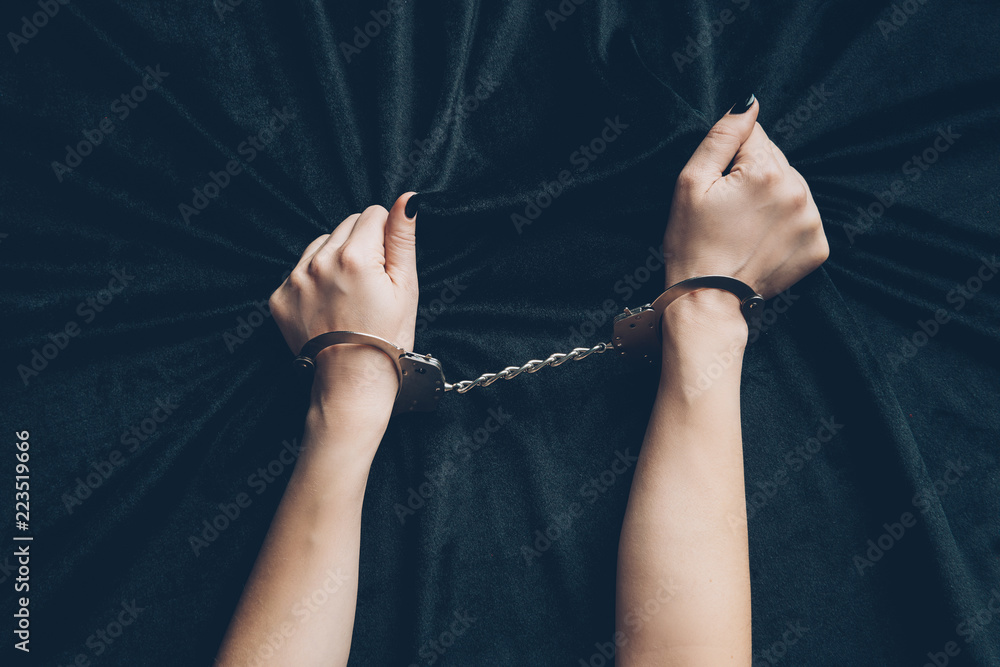 cropped shot of female hands in handcuffs holding black fabric - obrazy, fototapety, plakaty 