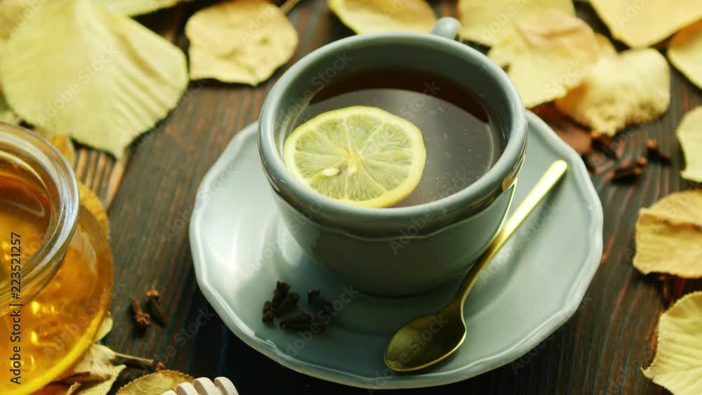 From above view of cup of hot tea with slice of lemon and bowl of honey placed near decorated with dry leaves on wooden background From above view of cup of hot tea with slice of lemon and bowl of honey placed near decorated with dry leaves on wooden background