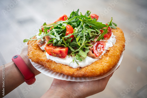 A young woman holding a traditional Hungarian Langos with cheese, rucola and tomatoes , Budapest, Hungury