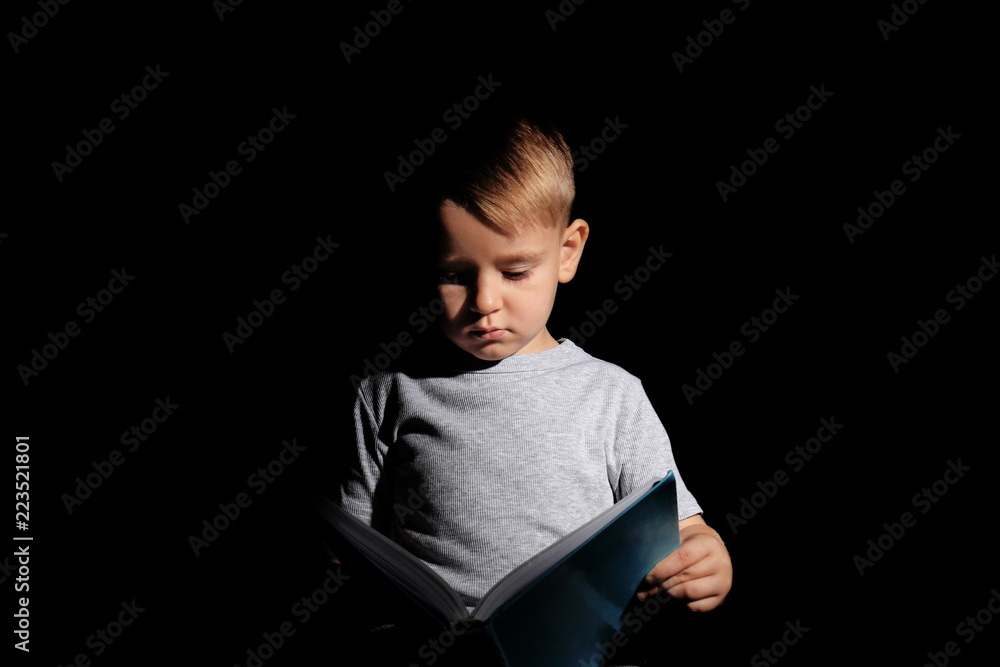 Cute little boy reading book on dark background Cute little boy reading book on dark background