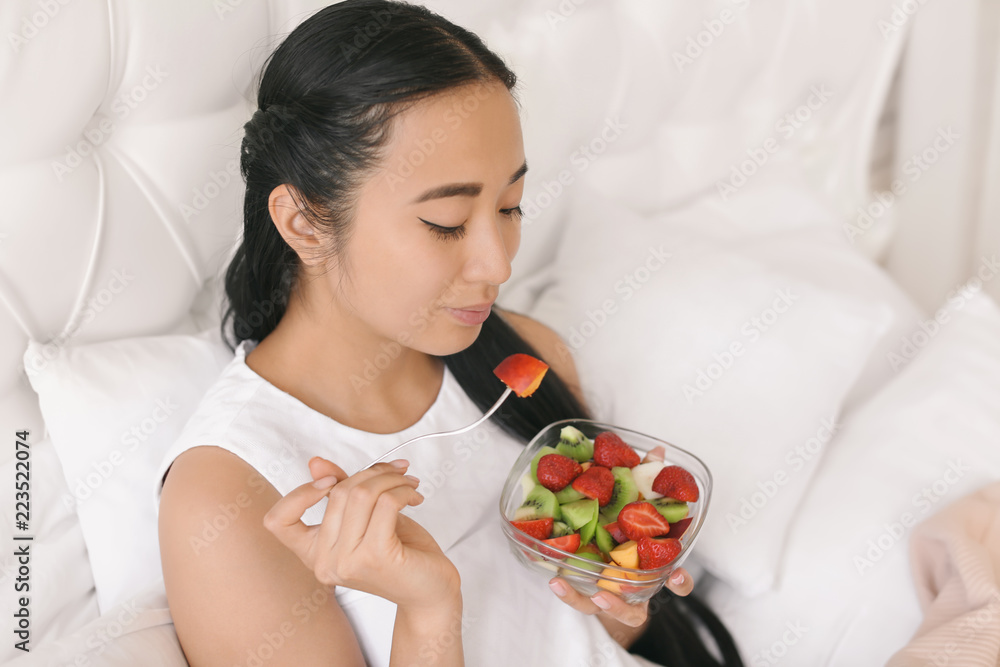 Asian woman eating healthy fruit salad for breakfast at home Asian woman eating healthy fruit salad for breakfast at home