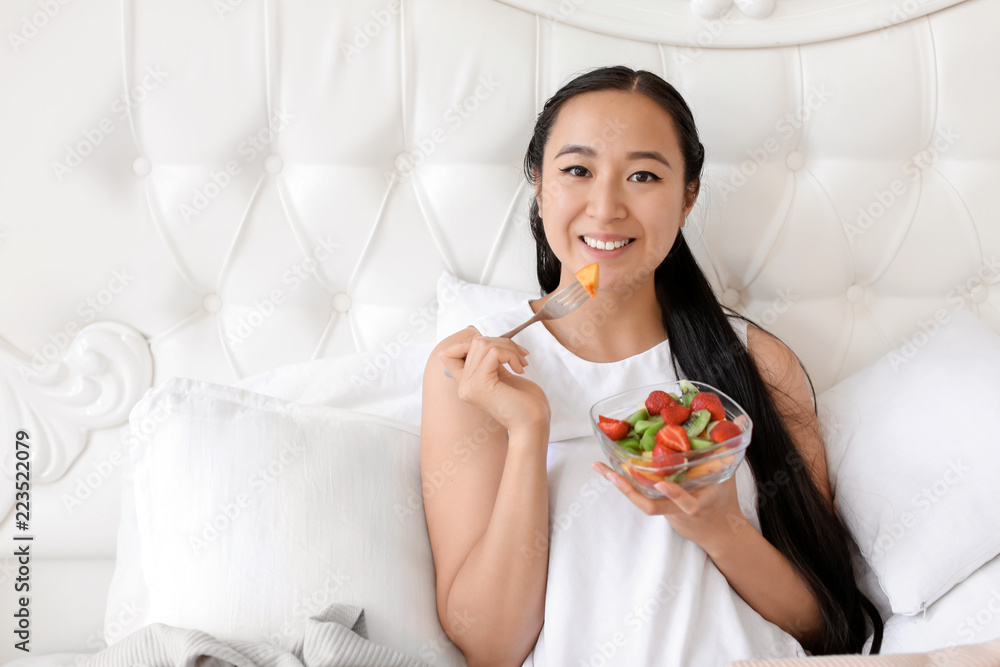 Asian woman eating healthy fruit salad for breakfast at home