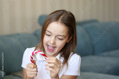 Beautiful happy smiling little girl holding Christmas candy cane and looking at it happily and excited. New Year coming