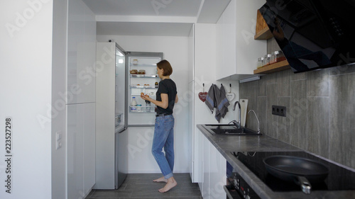 alone young woman is getting eggs from fridge in her kitchen in morning, preparing for cooking breakfast