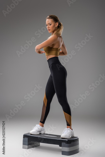 athletic young woman doing step aerobics on grey photo