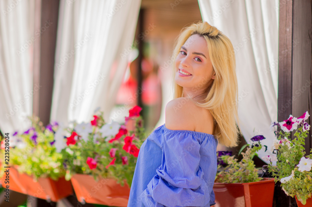 Portrait of happy beauiful young .tender woman with blond hair and pink make-up smiling on the background of flower pots. Summer portrait of a girl.