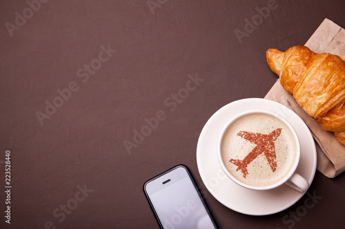 Mug of coffee with an airplane on the foam. Morning coffee with croissant in flight. Smrtrfonom and cup of coffee photo